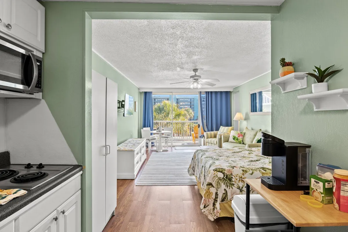 A welcoming interior shot featuring an open kitchen area adjacent to a comfortable seating space. The kitchen is modern and well-equipped, with a view extending toward the balcony, hinting at indoor-outdoor living. The arrangement allows for effortless movement between the kitchen, dining, and lounging areas.