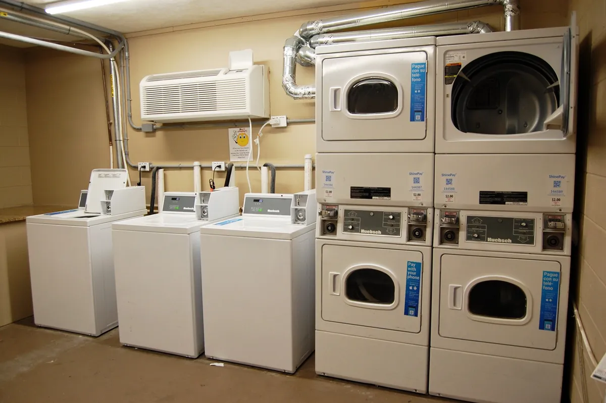 A clean, well-lit laundry area featuring several washing machines, dryers, and an air conditioning unit. The space is practical and organized, emphasizing ease and convenience for guests.