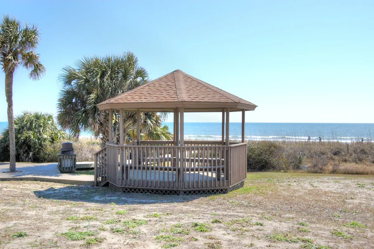 A gazebo with a panoramic ocean view sits in the foreground, surrounded by palm trees. The tranquil scene is perfect for relaxation, with the ocean visible in the distance, establishing the connection between the private balcony experience and the coastal environment.