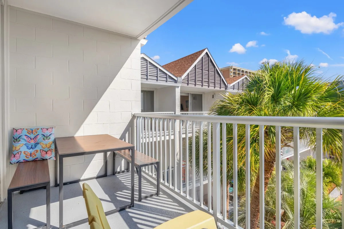 This image features a private balcony seating area framed by lush palm trees. Comfortable chairs are arranged for relaxation and conversation, and the setting overlooks greenery, invoking a peaceful ambiance. Soft natural lighting suggests morning or early evening, ideal times to enjoy coastal breezes.