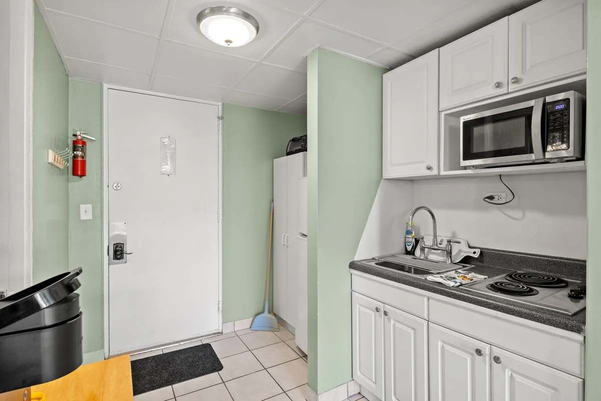 A compact, functional kitchenette with a sink, microwave, and refrigerator, located right by the entrance. The setup invites quick meal preparation, snacking, and casual mornings over coffee at the counter.