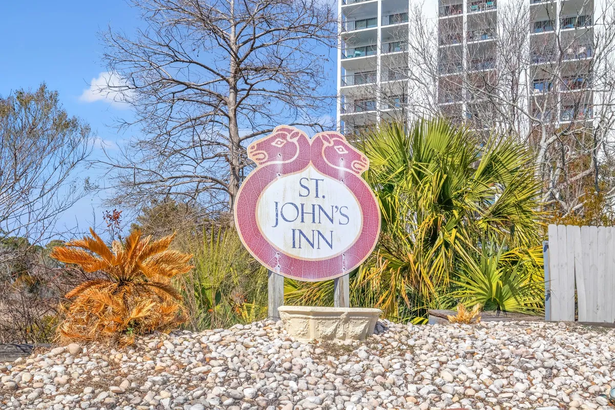An exterior view of St. John's Inn, framed by tropical palm trees and a well-kept pebbled landscape. The welcoming signage and inviting setting suggest a relaxing place to return to after a night out.